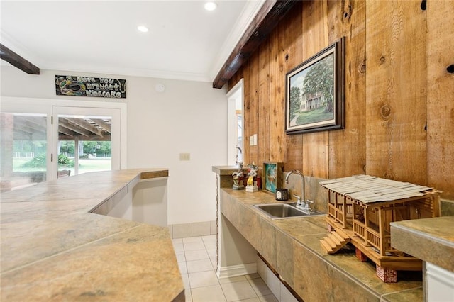 kitchen with light countertops, crown molding, a sink, light tile patterned flooring, and wooden walls