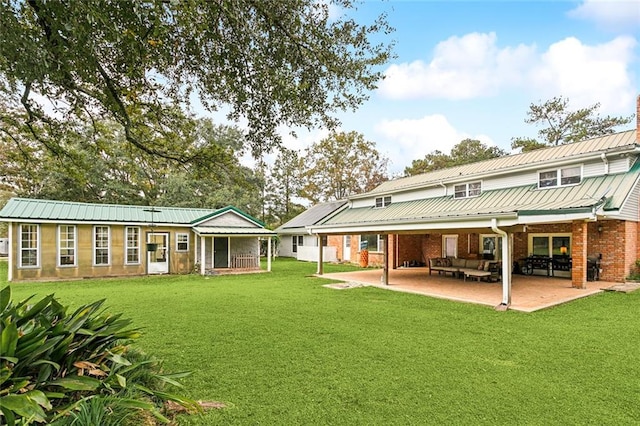 rear view of house with a standing seam roof, metal roof, brick siding, a yard, and a patio area