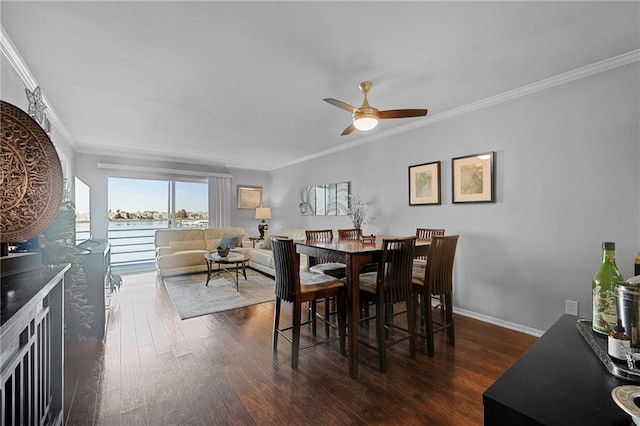 dining space featuring ceiling fan, a water view, ornamental molding, and dark wood-type flooring