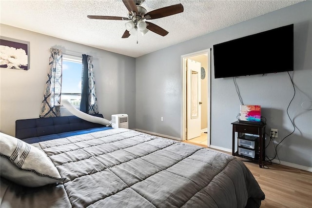 bedroom featuring light hardwood / wood-style floors, ceiling fan, ensuite bath, and a textured ceiling