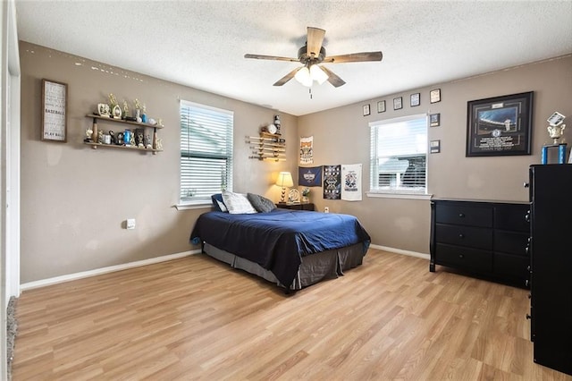 bedroom with a textured ceiling, multiple windows, ceiling fan, and light wood-type flooring