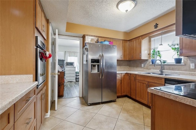 kitchen featuring a textured ceiling, sink, light tile patterned flooring, backsplash, and appliances with stainless steel finishes