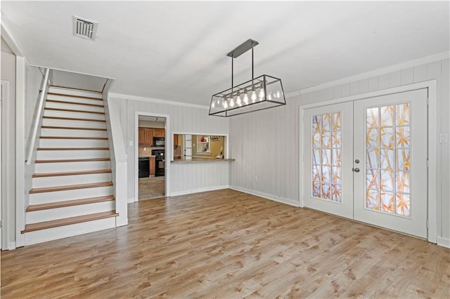 interior space featuring wood-type flooring, wooden walls, french doors, and ornamental molding