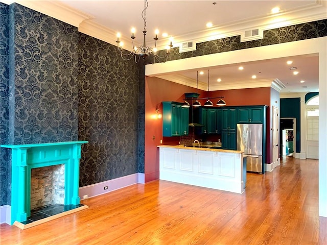 kitchen featuring stainless steel refrigerator, kitchen peninsula, crown molding, pendant lighting, and light wood-type flooring