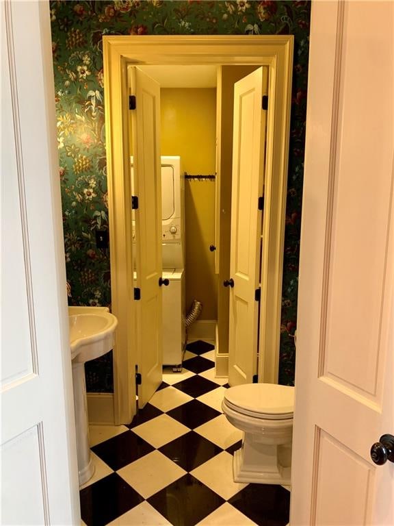 bathroom with stacked washer / drying machine and toilet