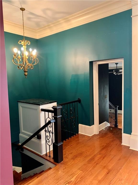 stairway featuring ornate columns, an inviting chandelier, ornamental molding, and hardwood / wood-style flooring