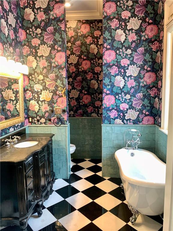 bathroom featuring a washtub, vanity, tile walls, and toilet