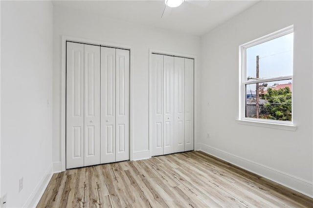 unfurnished bedroom featuring multiple closets, light hardwood / wood-style flooring, and ceiling fan