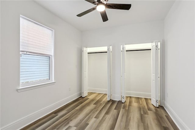 unfurnished bedroom featuring ceiling fan, light wood-type flooring, and two closets