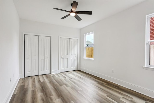 unfurnished bedroom featuring multiple closets, light hardwood / wood-style flooring, multiple windows, and ceiling fan