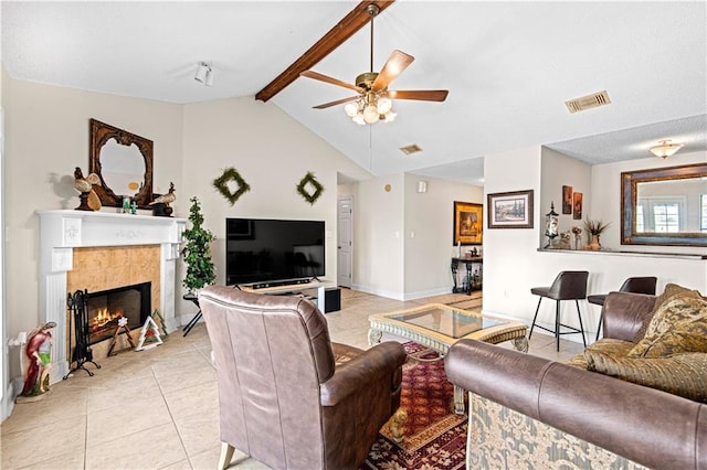 living room featuring vaulted ceiling with beams, ceiling fan, a tile fireplace, and light tile patterned floors