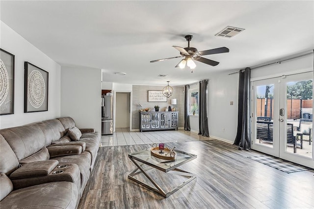 living room featuring french doors, light hardwood / wood-style floors, and ceiling fan with notable chandelier