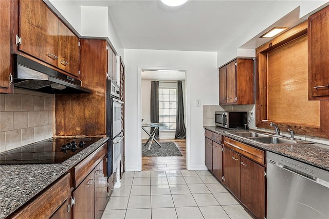 kitchen with dark stone countertops, sink, light tile patterned floors, and stainless steel appliances