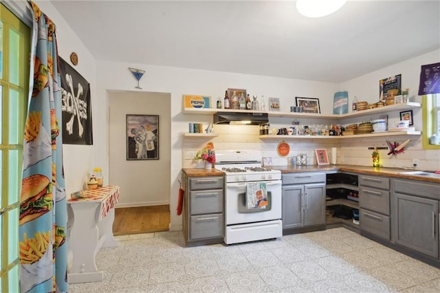 kitchen featuring gas range gas stove, a healthy amount of sunlight, light tile patterned floors, range hood, and gray cabinetry