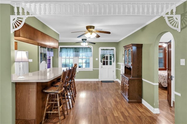 kitchen with kitchen peninsula, hardwood / wood-style floors, ornamental molding, and a breakfast bar