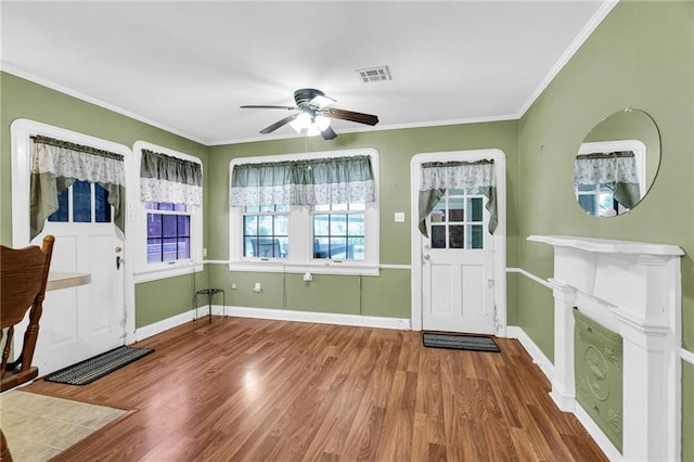 foyer with ceiling fan, wood-type flooring, a fireplace, and ornamental molding