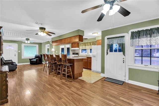 kitchen featuring ceiling fan, a breakfast bar, light wood-type flooring, and white refrigerator with ice dispenser