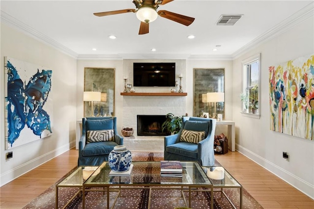 living room with ceiling fan, wood-type flooring, a brick fireplace, and crown molding