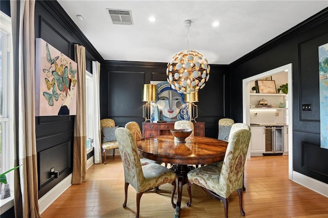 dining space featuring wine cooler, an inviting chandelier, crown molding, and light hardwood / wood-style flooring