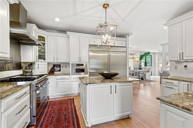 kitchen featuring white cabinets, wall chimney exhaust hood, high quality appliances, and a center island