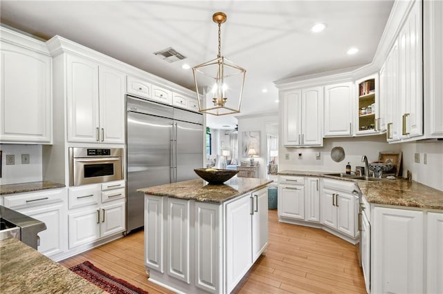 kitchen with stainless steel appliances, a center island, white cabinets, hanging light fixtures, and light wood-type flooring