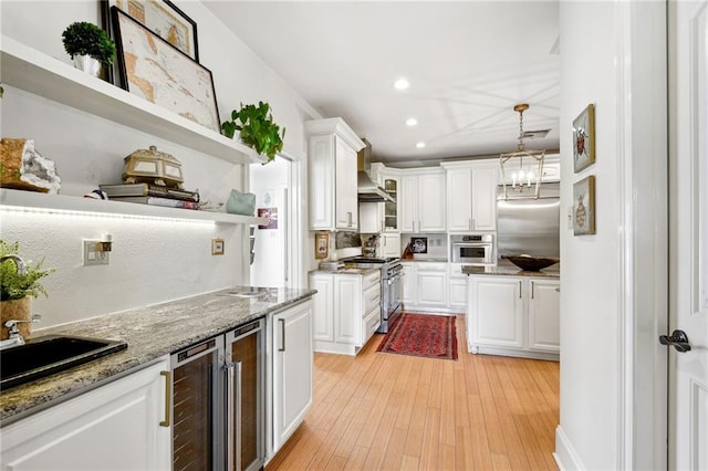 kitchen featuring high quality appliances, white cabinetry, light hardwood / wood-style flooring, decorative light fixtures, and wine cooler