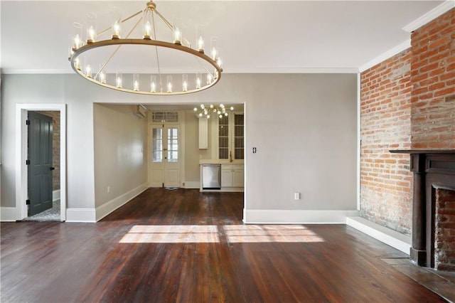 unfurnished dining area with a brick fireplace, a chandelier, crown molding, and dark hardwood / wood-style flooring