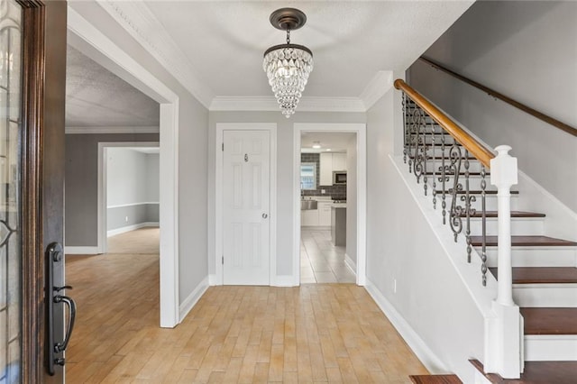 entryway featuring ornamental molding, light wood-type flooring, and a notable chandelier