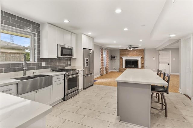 kitchen featuring a kitchen island, white cabinetry, appliances with stainless steel finishes, a large fireplace, and light hardwood / wood-style flooring