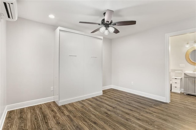 unfurnished bedroom with ensuite bathroom, ceiling fan, dark hardwood / wood-style floors, a closet, and an AC wall unit