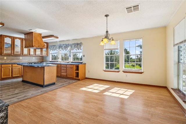 kitchen with light hardwood / wood-style floors, a textured ceiling, tasteful backsplash, a kitchen island, and decorative light fixtures