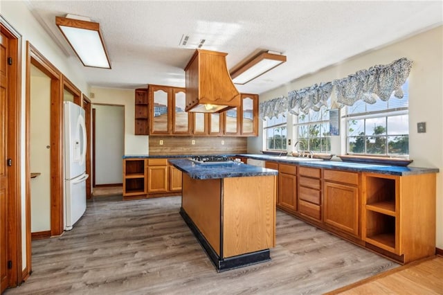 kitchen featuring premium range hood, a kitchen island, light wood-type flooring, white refrigerator, and backsplash