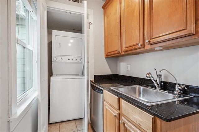 kitchen featuring stacked washer and clothes dryer, sink, dark stone counters, light tile patterned floors, and dishwasher