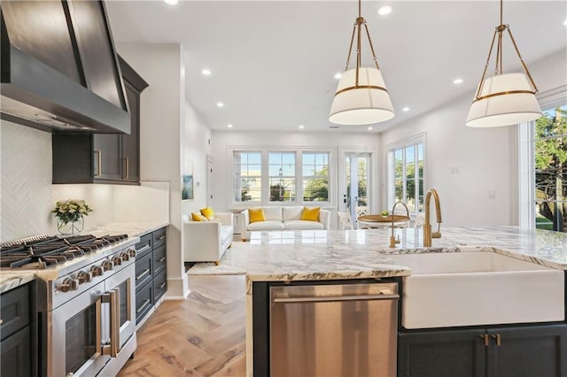 kitchen featuring pendant lighting, wall chimney range hood, sink, light parquet floors, and appliances with stainless steel finishes