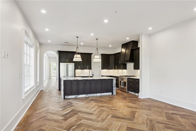 kitchen featuring premium range hood, high end appliances, decorative light fixtures, a kitchen island with sink, and light parquet floors