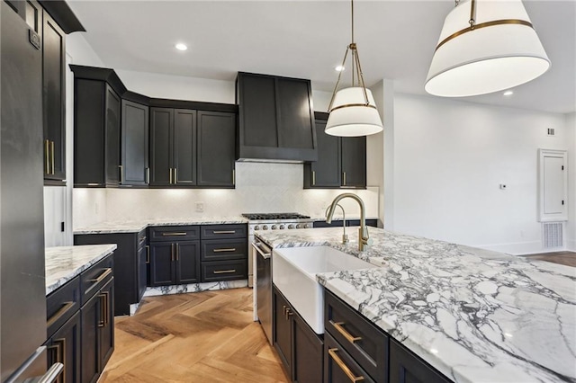 kitchen with wall chimney range hood, light parquet floors, hanging light fixtures, light stone countertops, and decorative backsplash