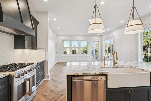 kitchen featuring sink, hanging light fixtures, stainless steel appliances, light parquet flooring, and wall chimney range hood