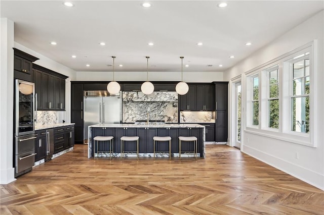 kitchen featuring hanging light fixtures, an island with sink, light parquet floors, and a breakfast bar