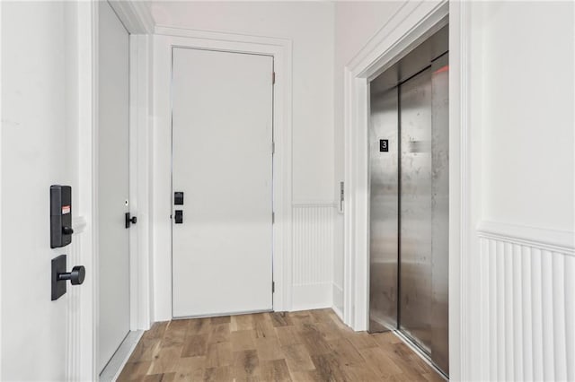 hallway with a decorative wall, wainscoting, elevator, and light wood-style flooring