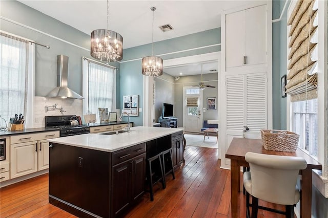 kitchen with black gas range oven, dark hardwood / wood-style floors, sink, decorative backsplash, and wall chimney exhaust hood