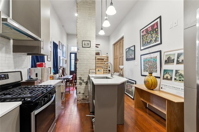 kitchen with sink, gas stove, dark hardwood / wood-style floors, decorative light fixtures, and an island with sink