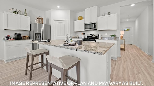 kitchen with stainless steel appliances, white cabinetry, light stone countertops, an island with sink, and light hardwood / wood-style floors