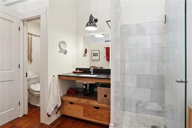 bathroom featuring wood-type flooring, vanity, toilet, and tiled shower