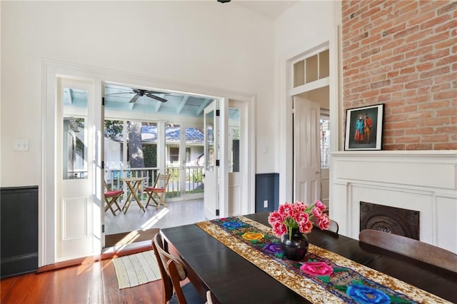 dining space featuring wood-type flooring, ceiling fan, and brick wall