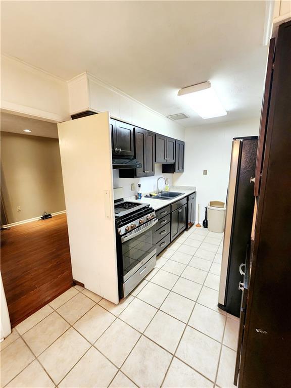 kitchen with refrigerator, stainless steel range with gas cooktop, sink, light tile patterned floors, and range hood