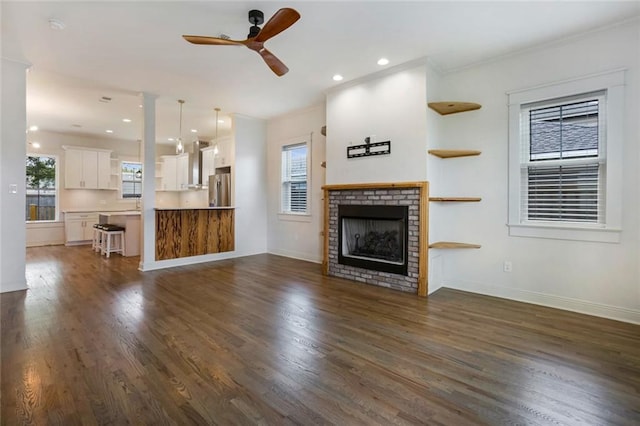 unfurnished living room featuring a fireplace, dark hardwood / wood-style flooring, plenty of natural light, and ceiling fan