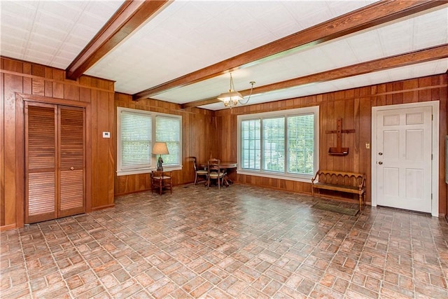 interior space featuring beamed ceiling, wooden walls, and a chandelier