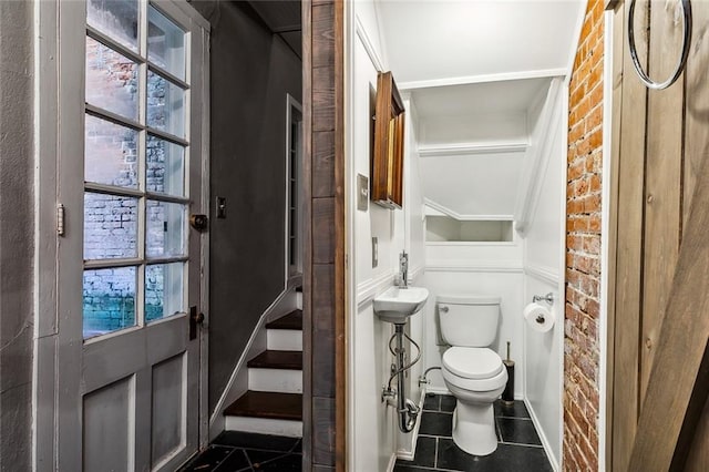 bathroom with sink, tile patterned flooring, brick wall, and toilet