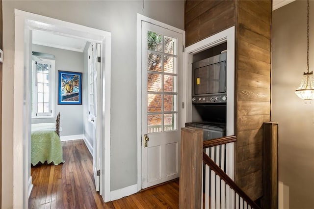 hallway with dark wood-type flooring, a wealth of natural light, stacked washer and clothes dryer, and ornamental molding