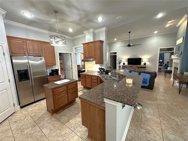 kitchen with ceiling fan with notable chandelier, a center island, sink, ornamental molding, and stainless steel fridge